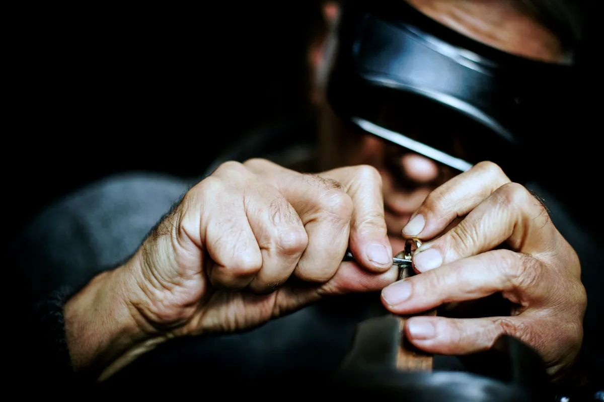 A jeweller in a head magnifier holding a small piece close to check it