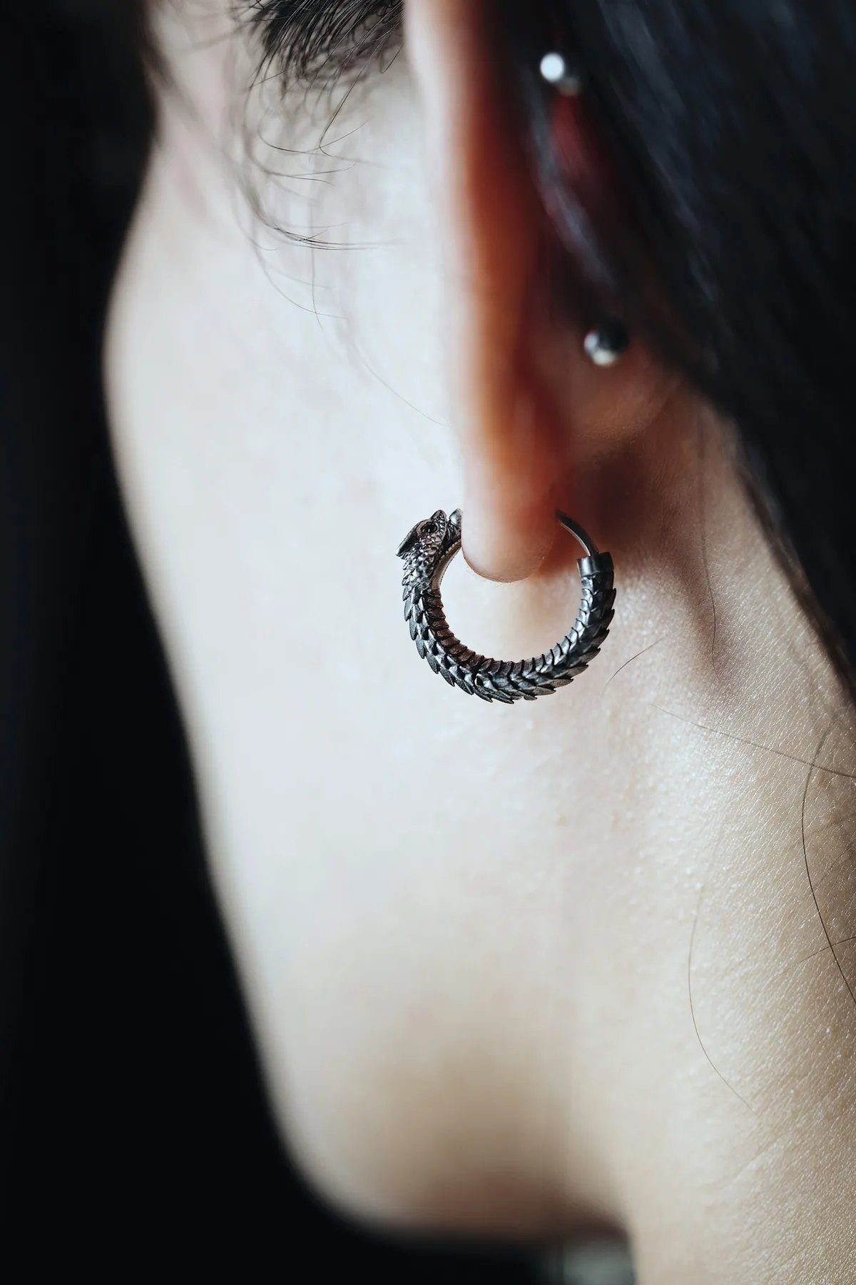 A textured silver hoop worn on the earlobe, against dark hair