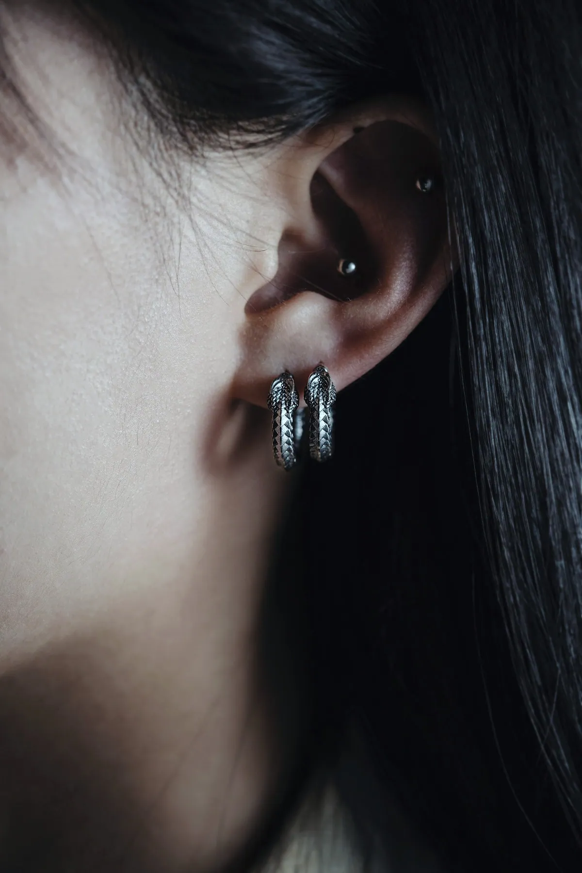 Two small textured silver hoops worn close together, framed by long dark hair