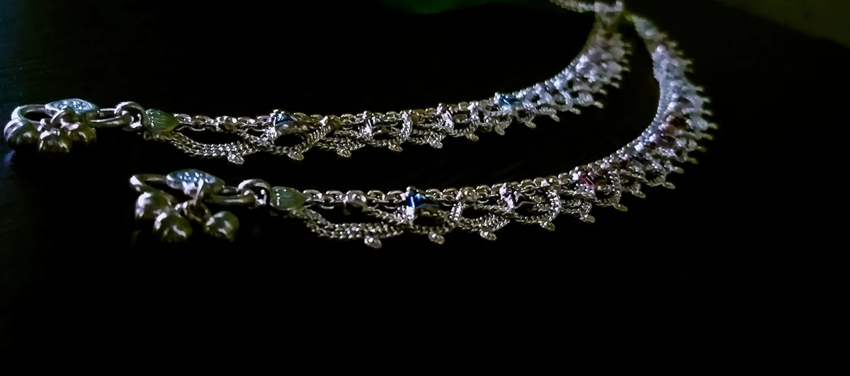 A pair of silver anklets with rows of tiny bells on a dark table