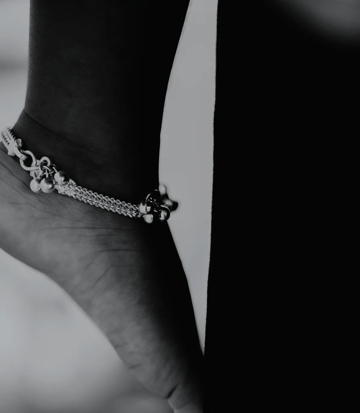 Black and white photo of a foot on tiptoe wearing a silver anklet with small bells