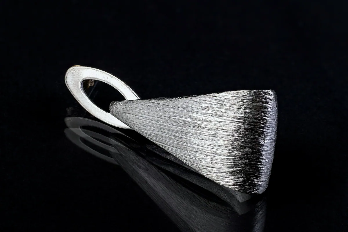 Close view of a brushed sterling silver pendant on black, its polished loop catching the light