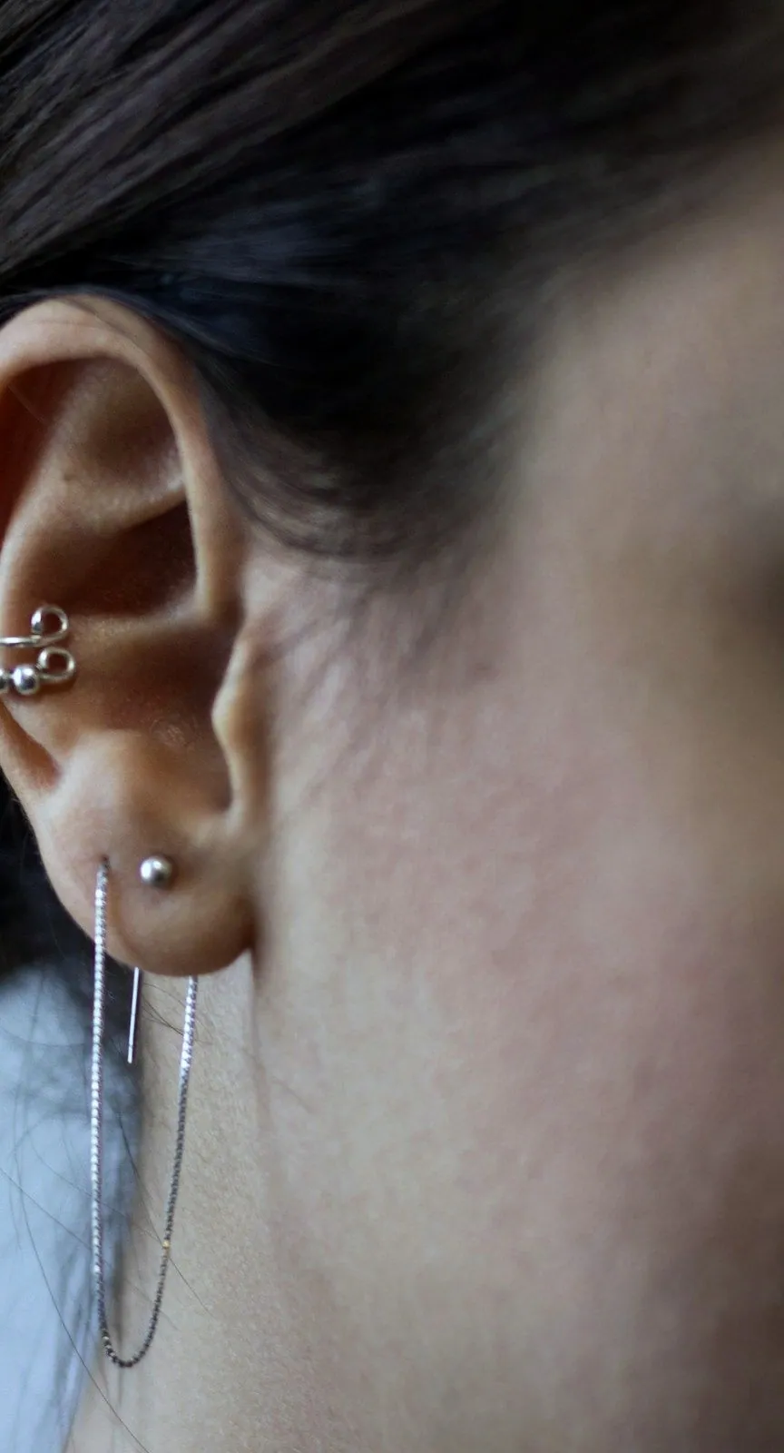 An ear with a slim silver cuff at the top and a fine chain drop below, against dark hair