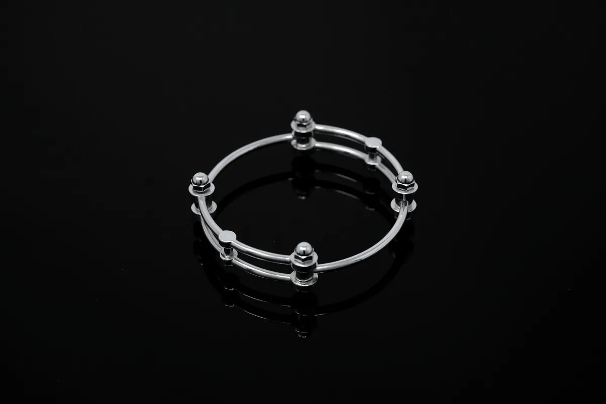 A silver bangle of two fine rods joined by small round beads, on a black reflective surface