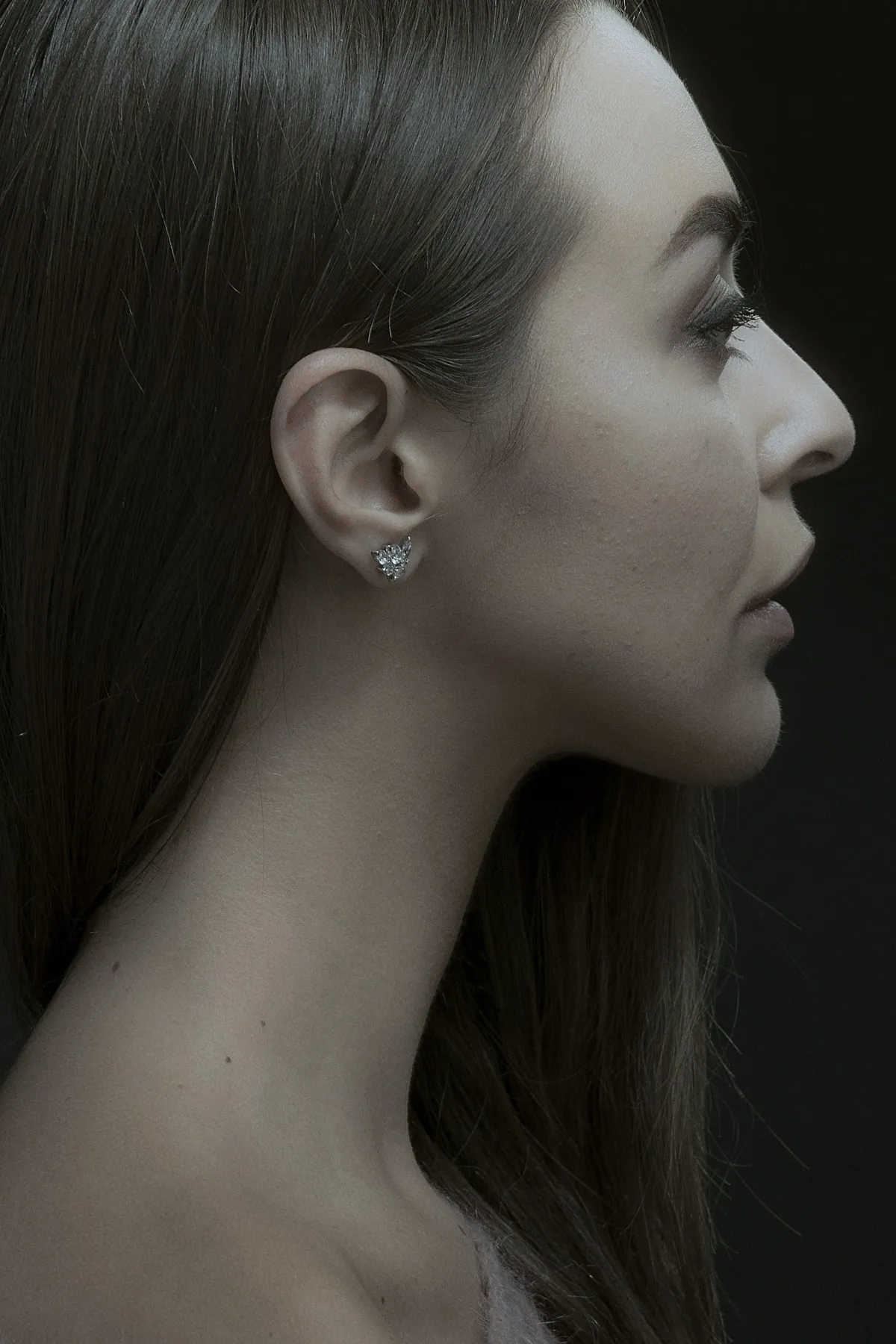 Profile of a woman against a dark background, wearing a small bright silver stud