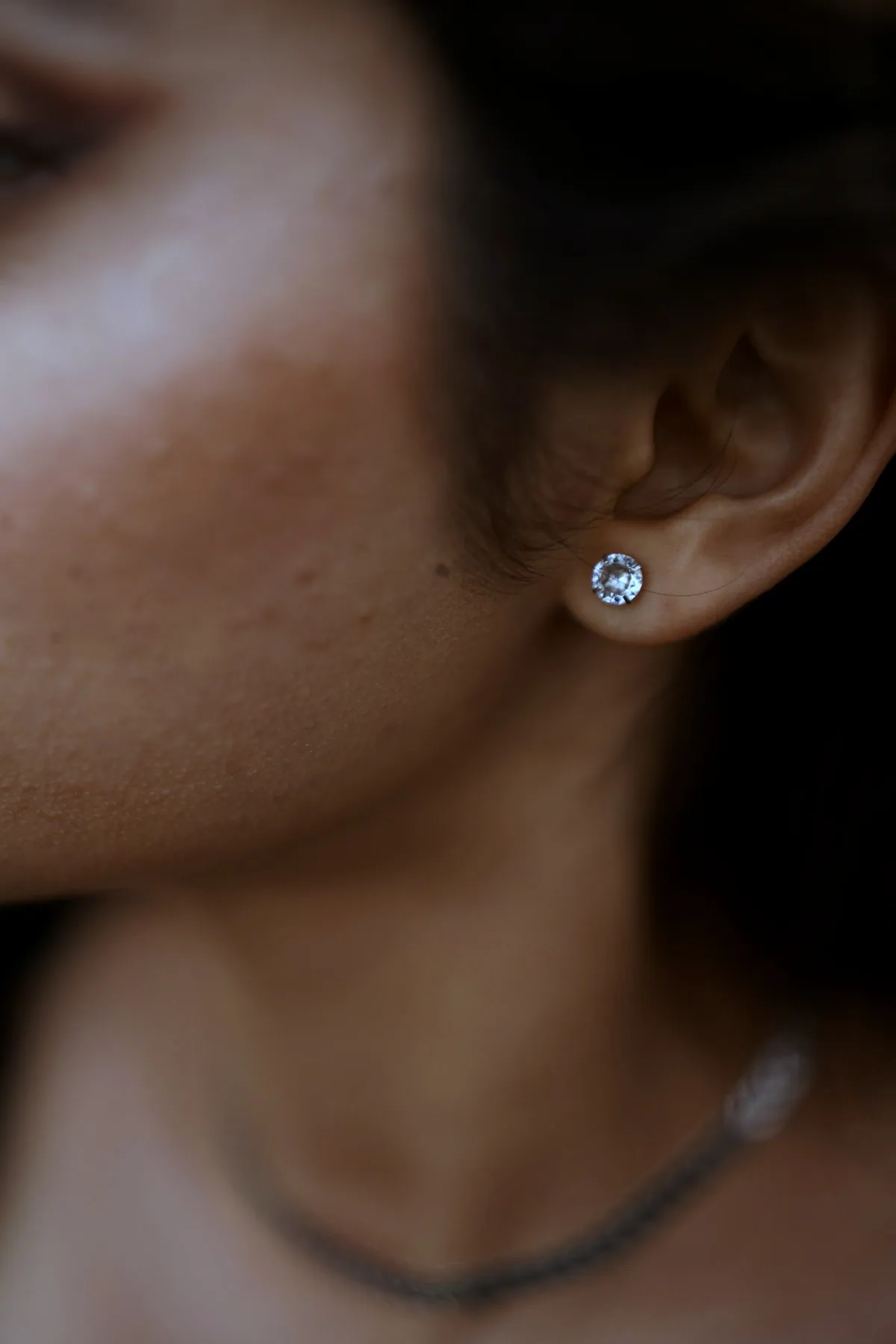 Close view of an ear wearing a small bright silver stud, in low light
