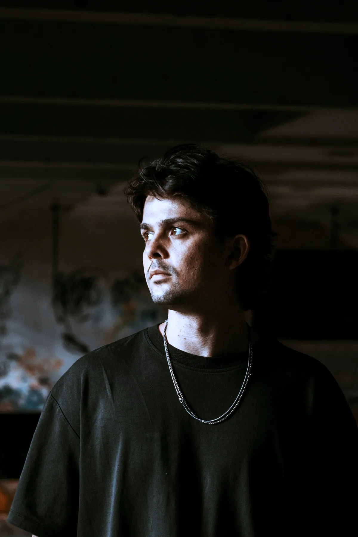 A man in a dark room wearing a black t-shirt and a long silver chain
