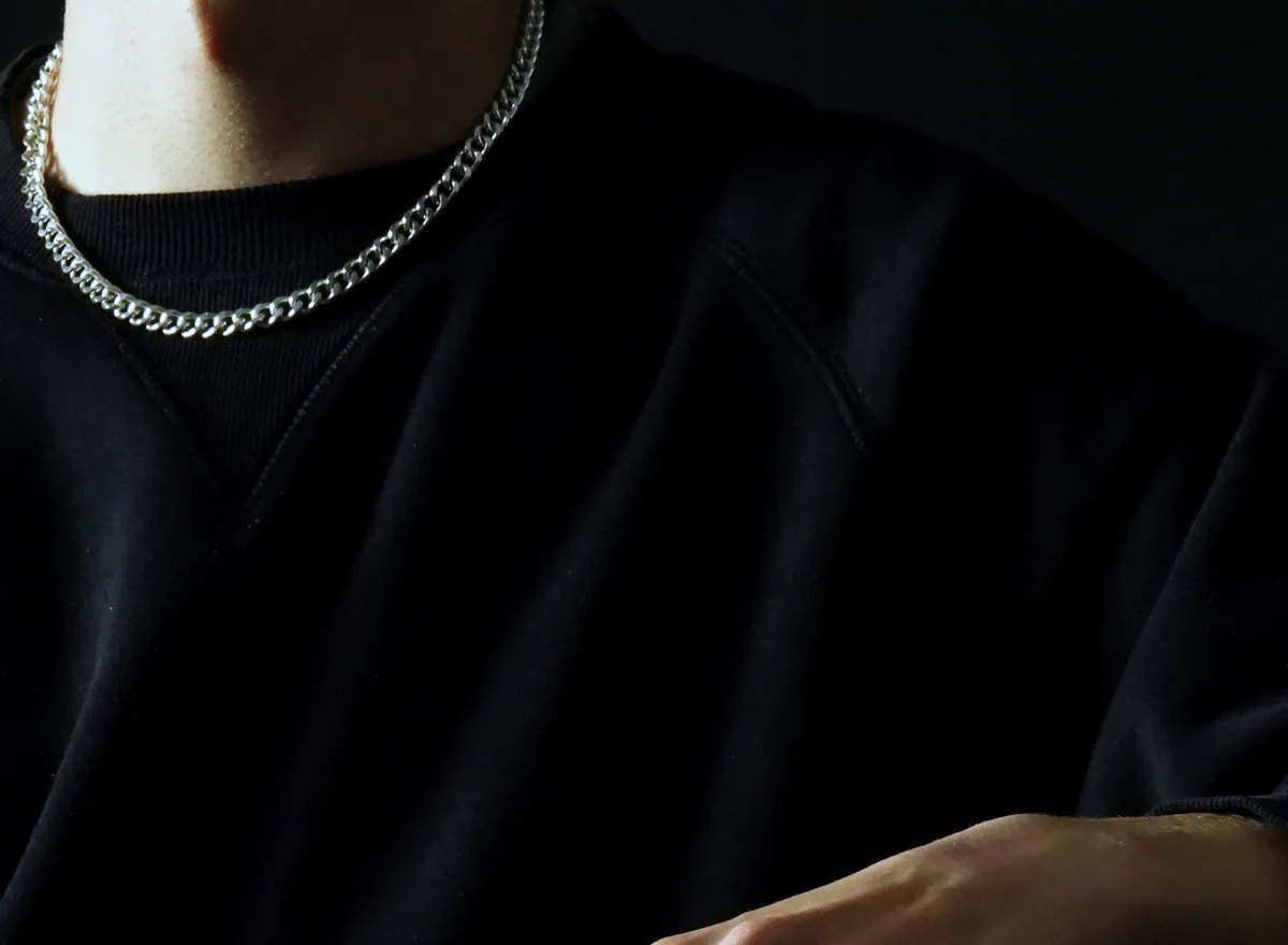 A silver link chain worn at the neck of a black sweatshirt