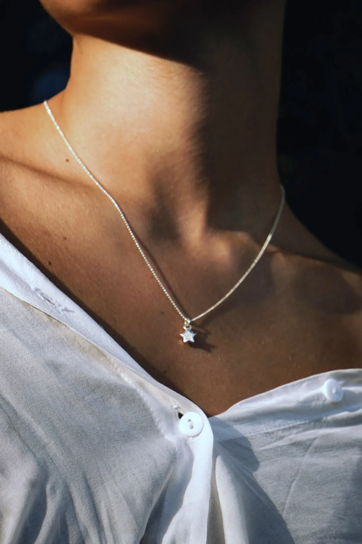 A small silver star pendant on a fine chain, worn with an open white shirt in low light
