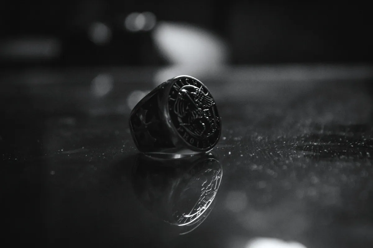 A heavy silver signet ring with an engraved face, reflected on a dark stone surface