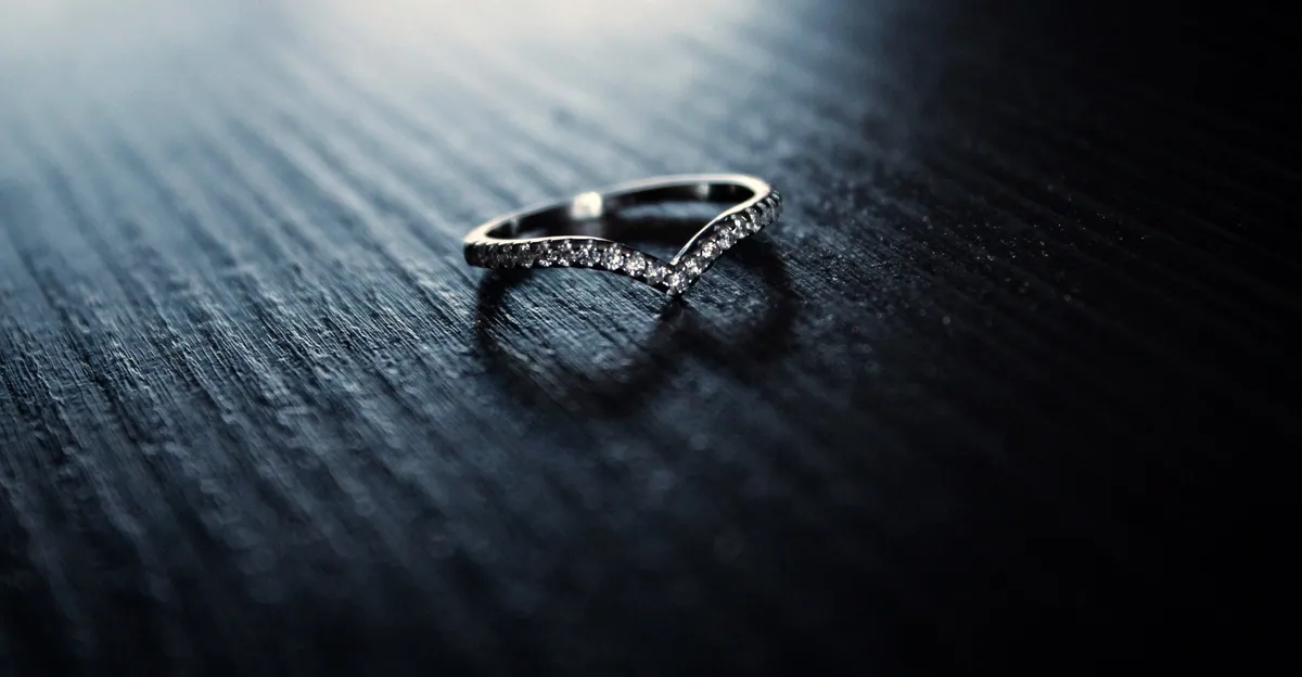 A fine silver ring that dips into a wave, on dark grained wood