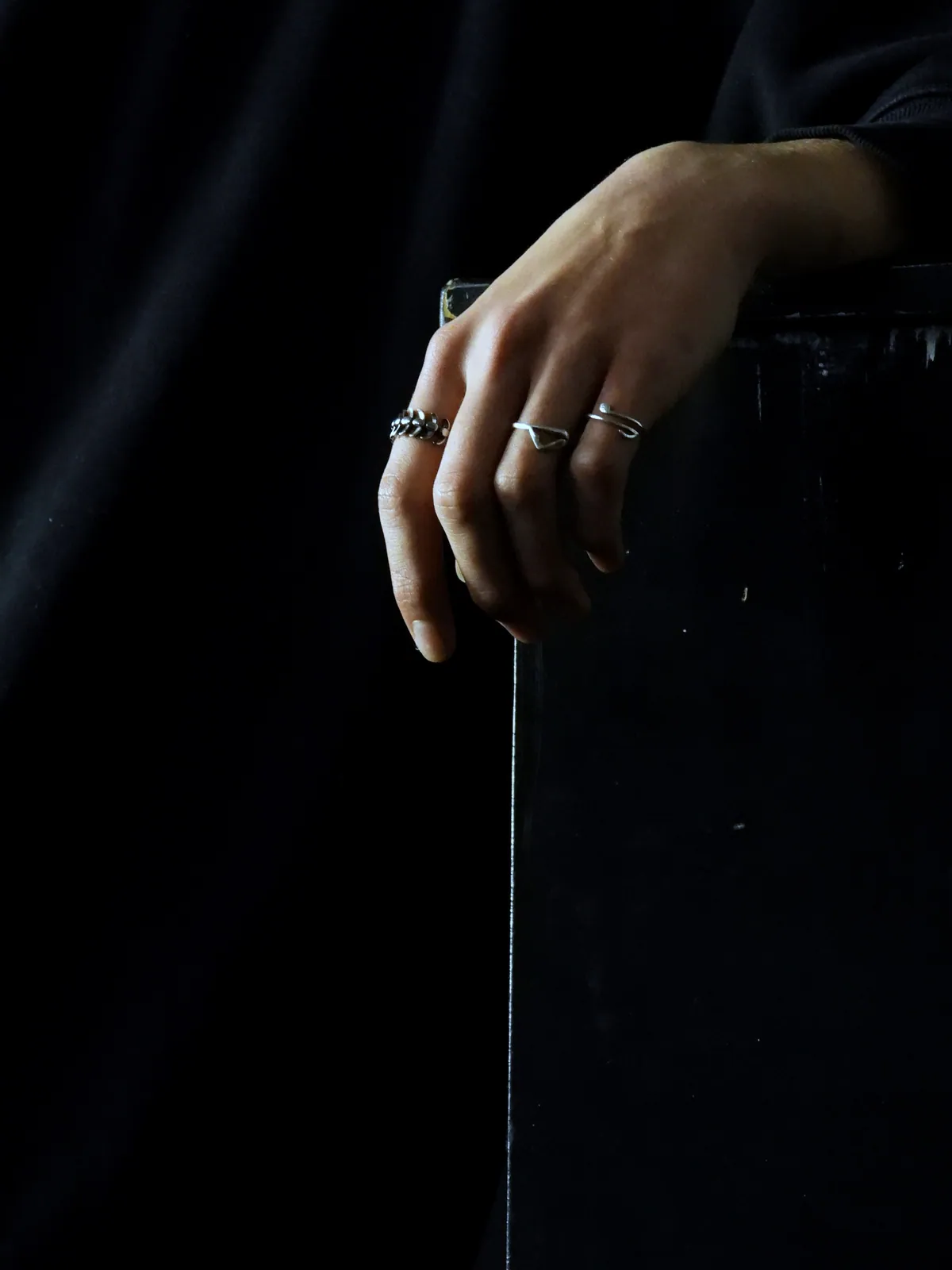 A hand resting on a black ledge wearing three slim silver rings, one with a wave